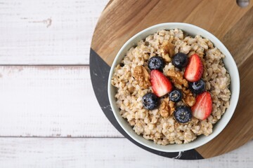 Tasty oatmeal with strawberries, blueberries and walnuts in bowl on white wooden table, top view