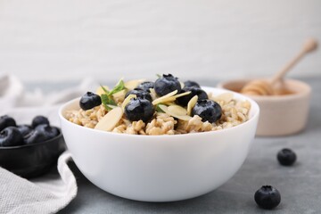 Tasty oatmeal with blueberries, mint and almond petals in bowl on grey table, closeup