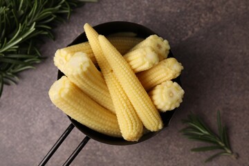 Tasty fresh yellow baby corns in dish on brown table, top view