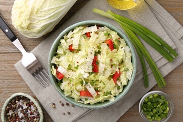 Tasty salad with Chinese cabbage in bowl, spices and ingredients on wooden table, flat lay