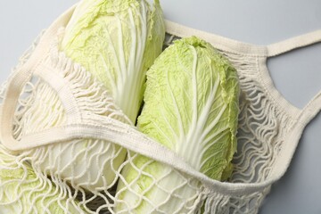 Fresh Chinese cabbages in string bag on light background, top view