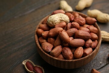 Fresh peanuts in bowl on wooden table, closeup. Space for text