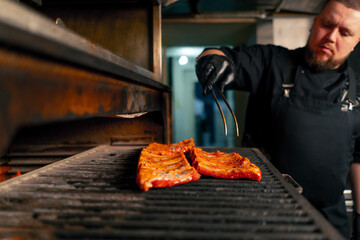 in a professional kitchen chef in a black jacket lays out marinated ribs near a hot grill oven
