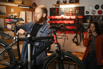 bearded mechanic and his wife repairing bicycle in a workshop.