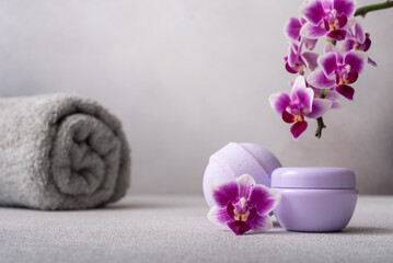 Fototapeta na wymiar Lilac cosmetic cream jar and bath ball on gray background with orchid flower