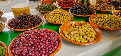 Shot showing a varied display of many types of fresh and dressed olives in wooden bowls, for sale at a supermarket or market