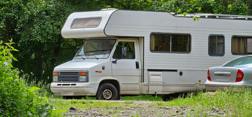 A motorhome parked in a forest car park; a campervan stopped in a woodland car park; RV in a forest car park.