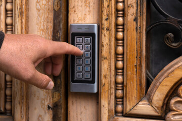 Hand presses keypad on wooden door. Metal combination lock. Close-up.