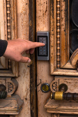 Hand presses keypad on wooden door. Metal combination lock.