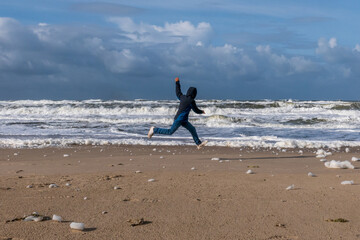 Ausgelassener Junge an einem Strand an der Nordsee an einem sonnigen und st&uuml;rmischen Tag