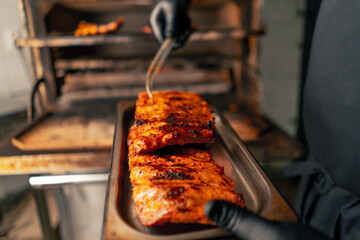 close-up of a professional kitchen chef in a black jacket near a hot grill oven takes ribs out of...