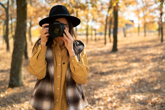 Woman tourist photographer taking photos of autumn yellow forest. Walking with camera in fall park.