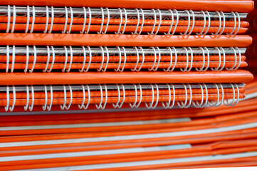 stack of orange notebooks with white spiral wire ties. coiled wire in book binding. printing...