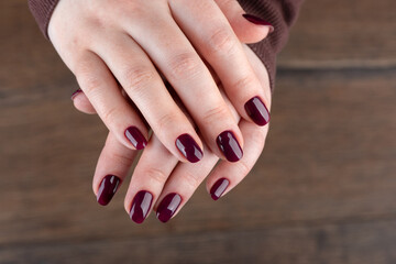 Female hands with blackberry-colored manicure over wooden background.