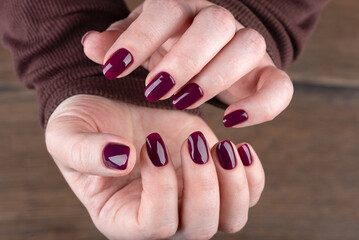 Blackberry colored manicure on female hands over wooden background.