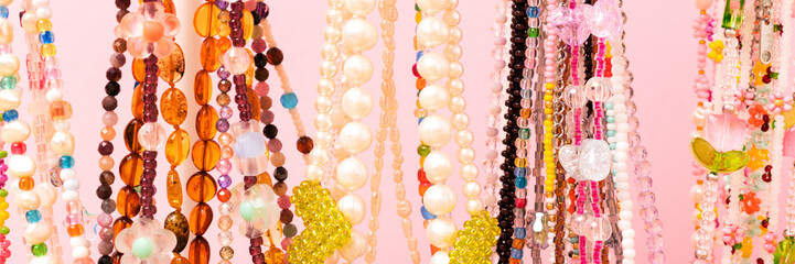 Banner with handmade chains of beads, pearls and natural stones in front of pink background.
