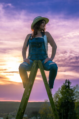 woman in dungarees sitting on a wooden ladder in the sunset