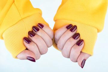 Female hands in a yellow jacket with a blackberry-colored manicure on the nails.