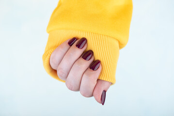 A woman's hand in a yellow jacket with a stylish blackberry-colored manicure.