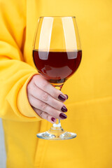 Close-up of a glass of wine in female hands with a stylish blackberry-colored manicure.