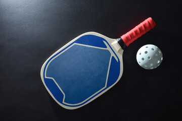 Pickleball paddle and white ball isolated on black table