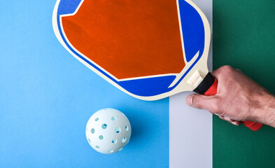 Hand with pickleball paddle on playing surface with white ball