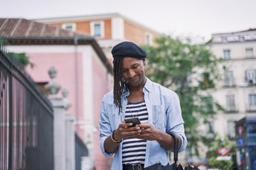 stylish young black man walking through the city using his mobile phone. he wears a beret and has...