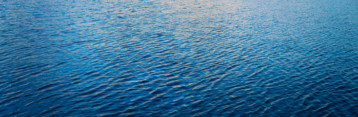 Water surface with small ripples and waves in wide angle banner format. Lake Powell at sunset with colorful sky reflections in shades of blue and yellow and color gradient. Background panorama.