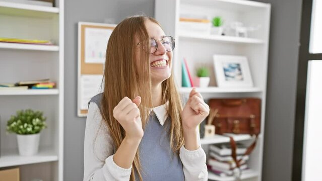 Exciting win! joyful young blonde business woman celebrates success at the office, arms raised, smiling, eyes closed - pure triumph!
