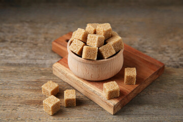 Brown sugar cubes in bowl on wooden table, closeup