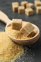 Spoon with brown sugar cubes on grey table, closeup