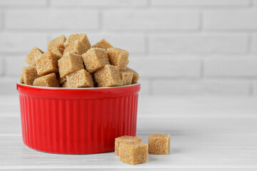 Brown sugar cubes in bowl on white wooden table, closeup. Space for text