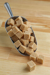 Brown sugar cubes in scoop on wooden table, closeup