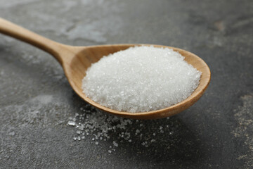 Spoon with granulated sugar on grey textured table, closeup