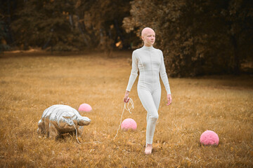Portrait of young hairless girl with alopecia in white cloth walking tardigrade toy in fall park,...