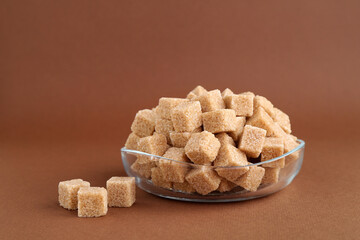 Brown sugar cubes in bowl on color background, closeup