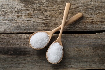 Organic salt in spoons on wooden table, flat lay