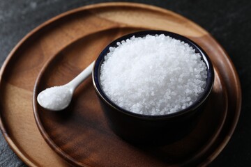 Organic white salt in bowl and spoon on black table, closeup