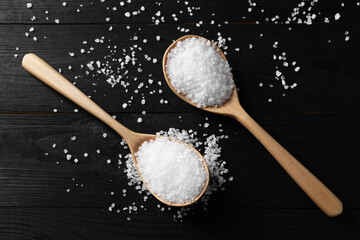 Organic salt in spoons on black wooden table, top view