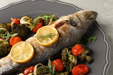 Baked fish with vegetables, rosemary and lemon on grey textured table, closeup