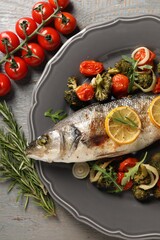 Baked fish with vegetables, rosemary and lemon on grey wooden table, flat lay