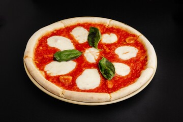 Freshly baked pizza with tomato sauce, basil, and melted cheese isolated on black background
