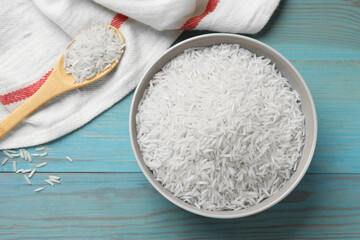 Raw basmati rice in bowl and spoon on light blue wooden table, flat lay