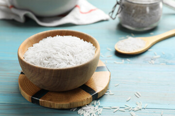 Fototapeta na wymiar Raw basmati rice in bowl on light blue wooden table, closeup. Space for text