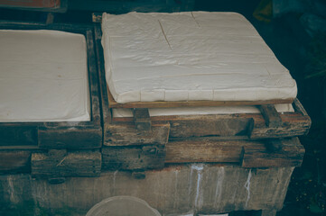 Overhead view of soy curd being pressed into wooden mold in a traditional Indonesian tahu or tofu...