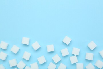 Fototapeta na wymiar White sugar cubes on light blue background, top view. Space for text