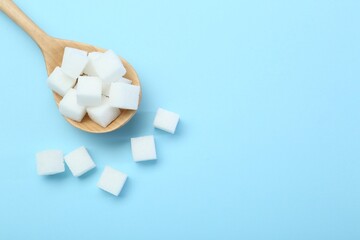 White sugar cubes and wooden spoon on light blue background, top view. Space for text