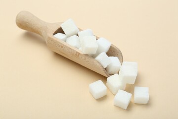 White sugar cubes and wooden scoop on beige background
