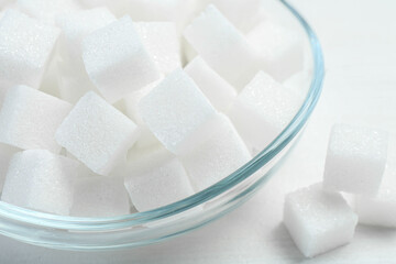 Many sugar cubes in glass bowl on white wooden table, closeup