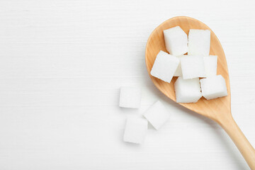 Many sugar cubes and wooden spoon on white table, top view. Space for text